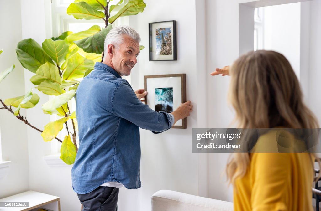 Pareja en casa colgando un cuadro enmarcado en la pared