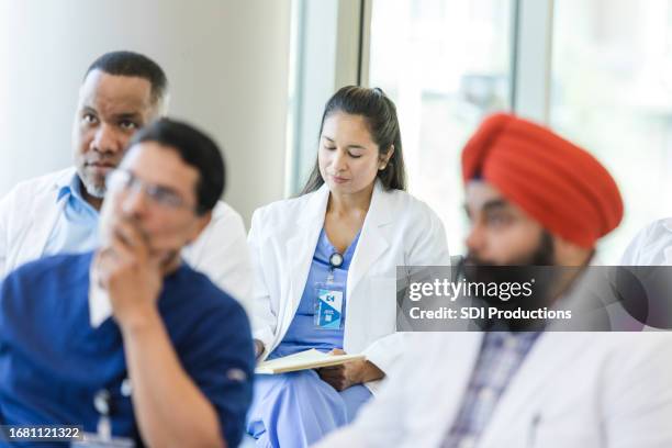 focus on female doctor sitting in back row of classroom - american college of physicians stock pictures, royalty-free photos & images