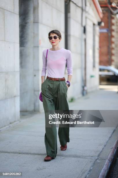 Guest wears sunglasses, a pink top, brown leather belt, green pants, brown shoes, a purple bag, outside Gabriela Hearst, during New York Fashion...