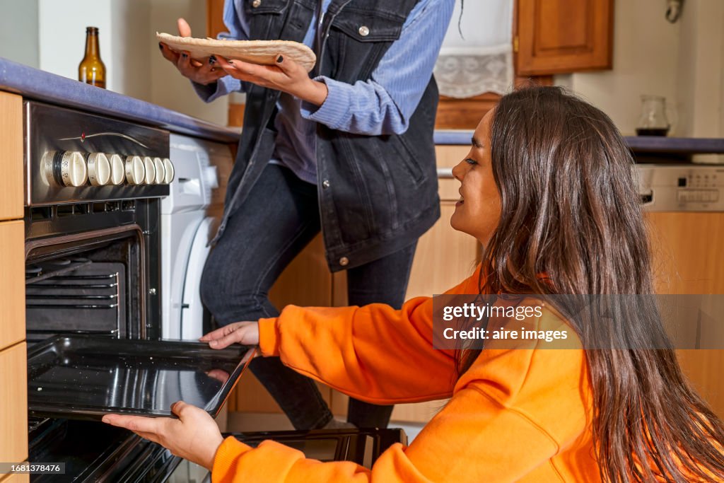 Two friends women preparing pizza togetherness in domestic kitchen at home