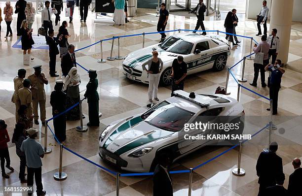 People look at the Aston Martin One-77 and Mercedes SLS on display during the Arabian Travel Market at the Dubai World Trade Centre in the Emirati...