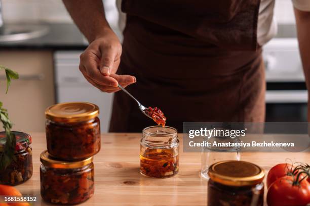 a man cans sun-dried tomatoes in glass jars on a wooden table - kazakhstan food stock pictures, royalty-free photos & images