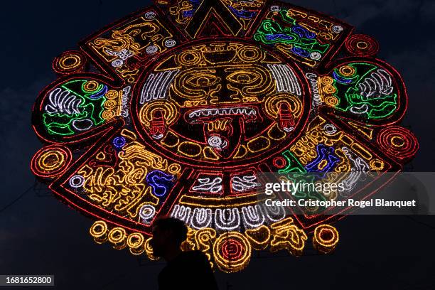 Person walks by a giant illuminated decoration of the Aztec sun stone ahead of the celebrations of El Grito de Dolores and the Independence Day on...