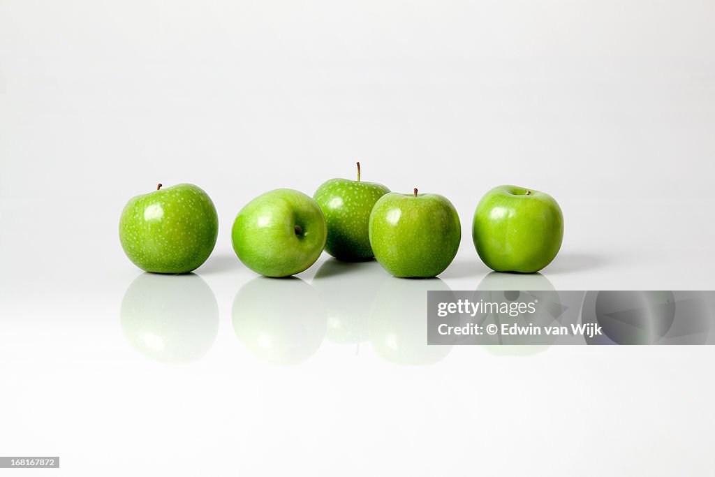 Five green apples on a light grey background