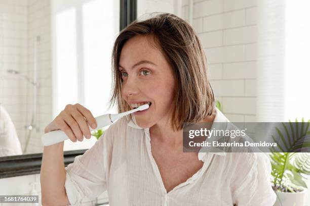 woman brushing her teeth with an electric brush in bathroom at home - brushing teeth stock pictures, royalty-free photos & images