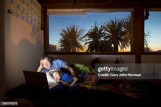 father and son using technology at night in bed - child's bedroom stock-fotos und bilder