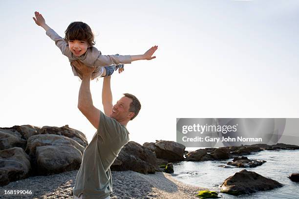 dad lifts young son above his head on beach - 息子 ストックフォトと画像