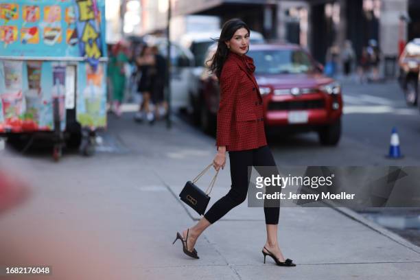 Kate Bartlett is seen wearing a black satin hairband, golden earrings, a buttoned blazer in red/black houndstooth pattern, the matching bow tie, a...