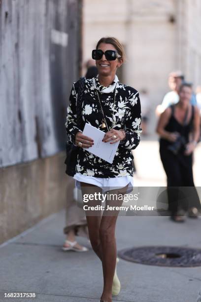 Fashion show guest is seen wearing light beige and green shoes, white shorts, a black braided bag, dark sunglasses and a black pullover with...