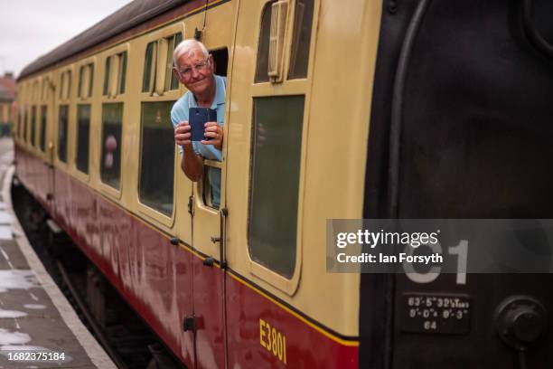 Man leans from a carriage window taking pictures as he departs from the North Yorkshire Moors Railway station at Pickering on September 15, 2023 in...