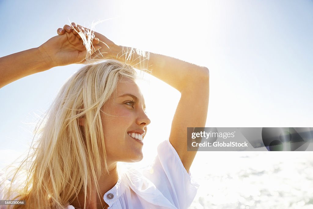 Young woman smiling with hands over head on beach