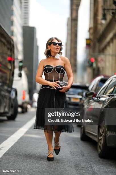 Olga Ferrara wears sunglasses, a choker with a white flower attachment, a black and white mesh corset, a black tulle pleated mesh skirt, high heels...