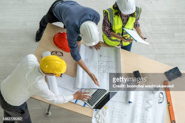 high-angle photo from directly above of an architect, a businessman, and a construction worker examining a blueprint on a construction site. - architect on site stock pictures, royalty-free photos & images