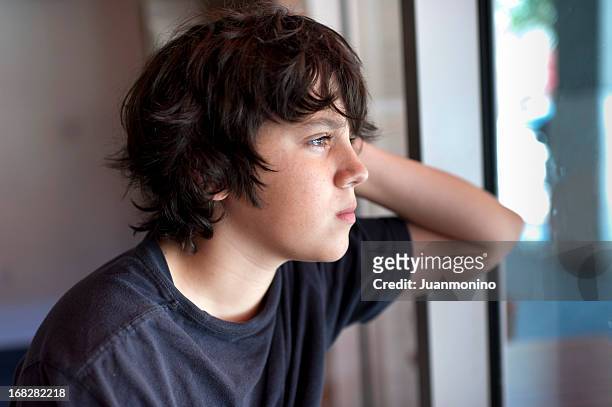 enfant pensif regardant à travers une fenêtre - élève 12 ans photos et images de collection
