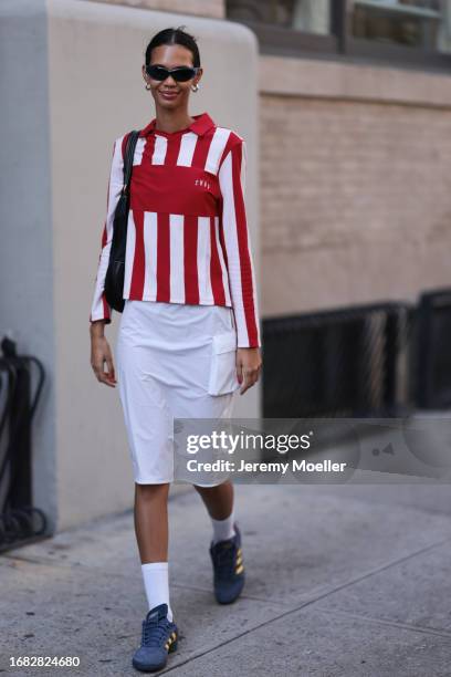 Guest is seen outside Brandon Maxwell show wearing blue sunnies, silver hoop earrings, white and red striped shirt, white midi cargo skirt and blue...