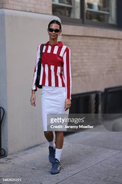 Guest is seen outside Brandon Maxwell show wearing blue sunnies, silver hoop earrings, white and red striped shirt, white midi cargo skirt and blue...