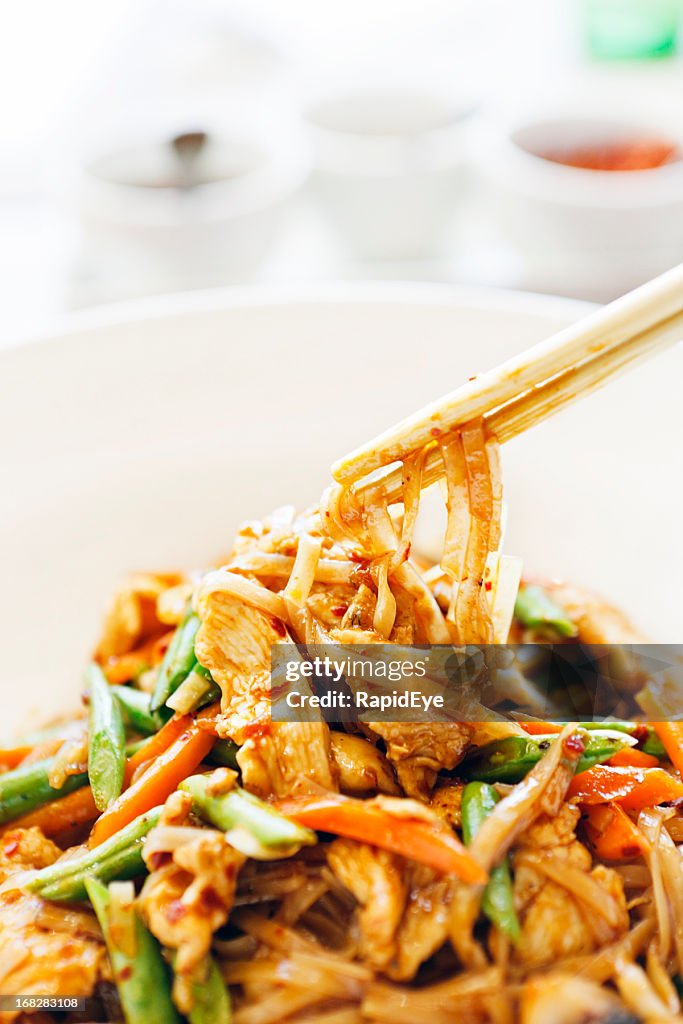 Chopsticks taking stir-fried Thai chicken with noodles from bowl