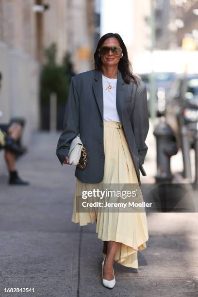 Guest is seen outside Brandon Maxwell show wearing brown aviator shaped sunnies, white shirt, golden old Celine letter necklace, grey oversized...