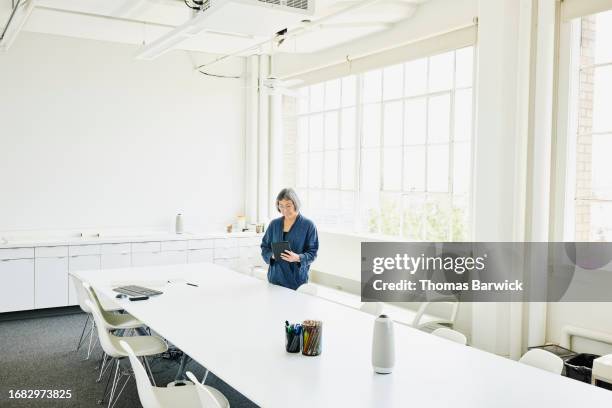 wide shot businesswoman working on digital tablet in conference room - high key stock-fotos und bilder