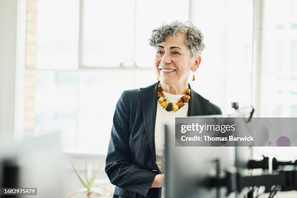 medium shot senior businesswoman in discussion at workstation in office - high key photos et images de collection