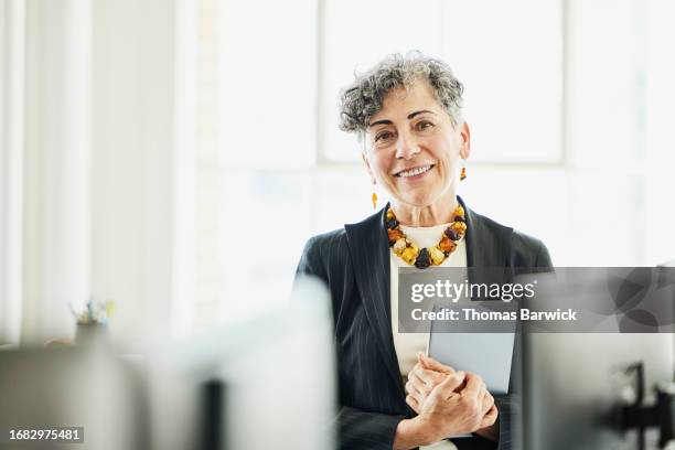 medium shot smiling senior businesswoman at workstation in office - halbnahe-einstellung stock-fotos und bilder