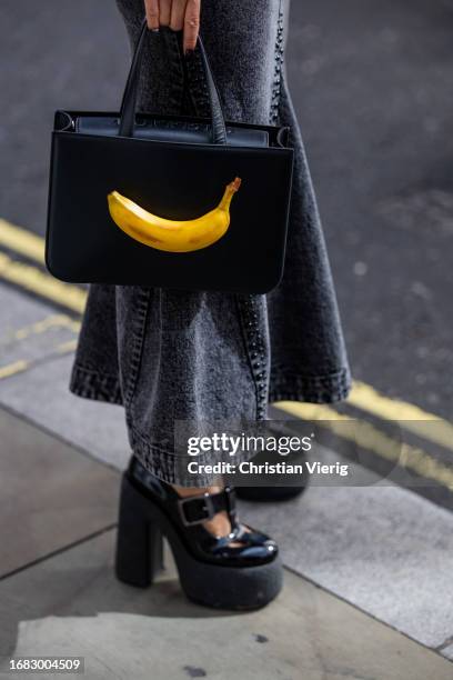 Betty Bachz wears cap, bag with banana, grey denim skirt, ruffled black blouse outside Huishan Zhang during London Fashion Week September 2023 on...