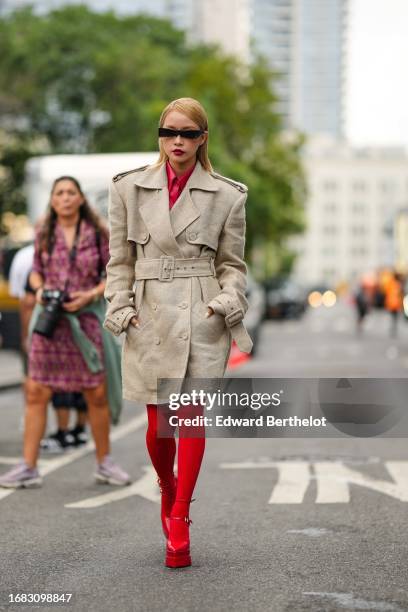 Guest wears sunglasses, a red shirt, a beige trench coat, red tights, platform pointed shoes, outside Michael Kors, during New York Fashion Week, on...