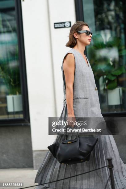 Guest wears Lanvin sunglasses, a gray oversized sleeveless jacket, a long pleated skirt, a black leather large bag, outside Michael Kors, during New...