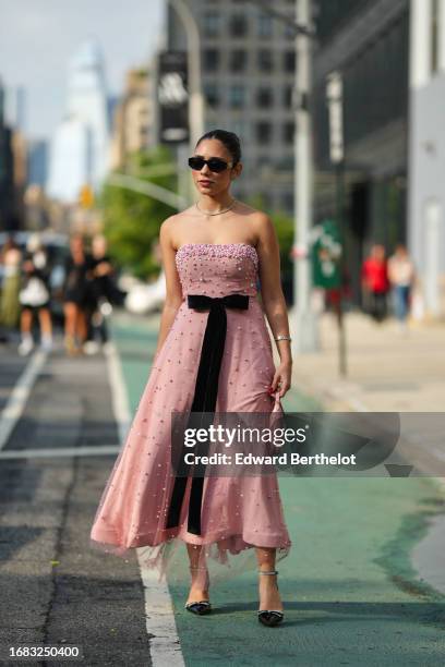 Guest wears sunglasses, a necklace, a pink off-shoulder midi dress with tulle attached pearls / beaded, a long black bow-tie mid attachment, black...