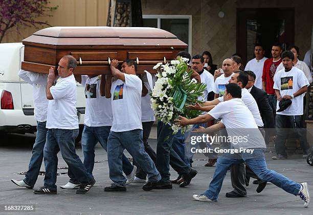 Pallbearers carry the casket of Ricardo Portillo out of a family viewing as two people catch flowers that fell off the casket as it is carried to a...