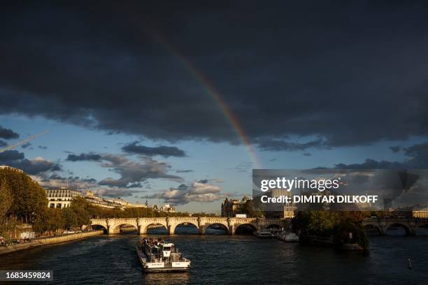 Boat cruises on the Seine river with a rainbow in background near The Pont Neuf bridge in Paris on September 22, 2023.