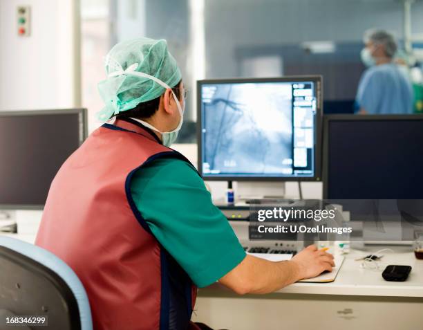 cardiologist with a mask looking at an x-ray on computer - angioplasty stock pictures, royalty-free photos & images