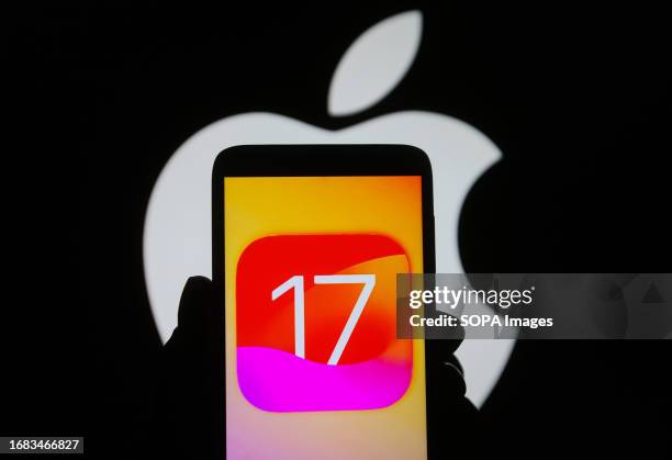 In this photo illustration, iOS 17 logo is seen on a smartphone and an Apple logo on a pc screen in the background.