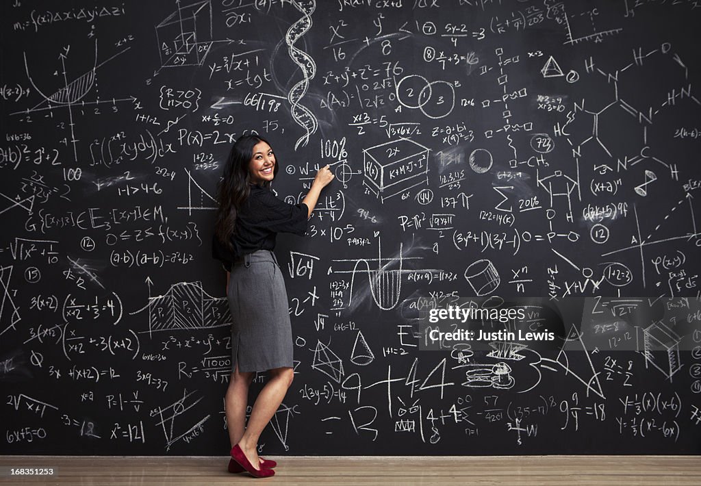 Young woman writes math equations on chalkboard