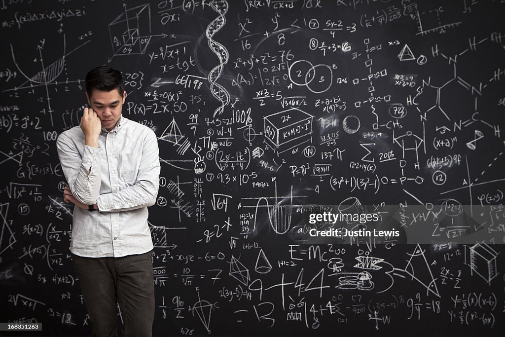 Man stands thinking in front of math chalkboard
