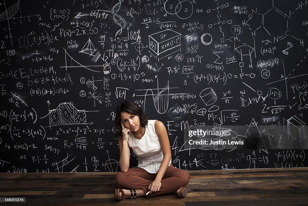 Young girl sits by mathematical chalkboarda