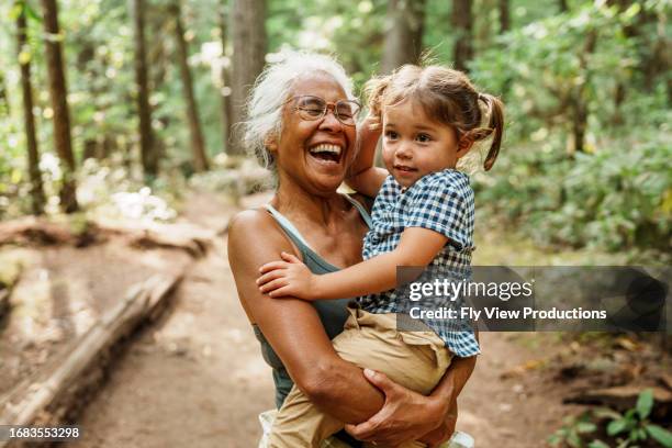 vibrant pacific islander senior woman hiking with eurasian granddaughter - aziatische etniciteit stockfoto's en -beelden