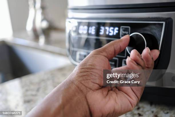 woman adjusts temperature on air fryer - airfryer stock-fotos und bilder