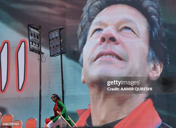 Supporter of Pakistani politician and former cricketer Imran Khan walks onto a stage next to an electoral poster of Khan at the venue of an election...