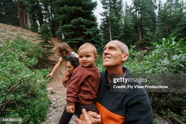 curious senior man carries grandson while hiking on a forest trail - hiking pacific northwest stock pictures, royalty-free photos & images