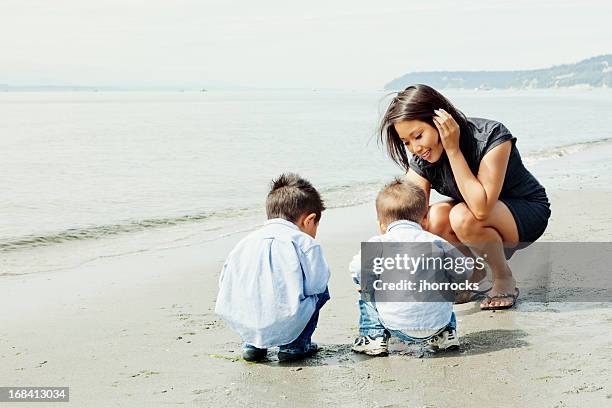 mother and curious sons crouching on seattle beach - seattle people stock pictures, royalty-free photos & images