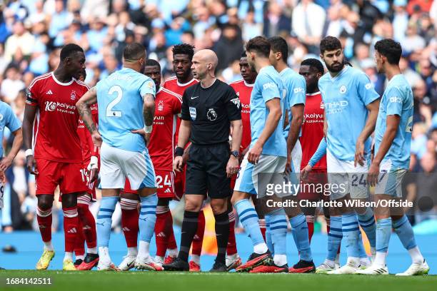 Referee Anthony Taylor is surrounded by players form both teams as they await a VAR decision for a red card during the Premier League match between...
