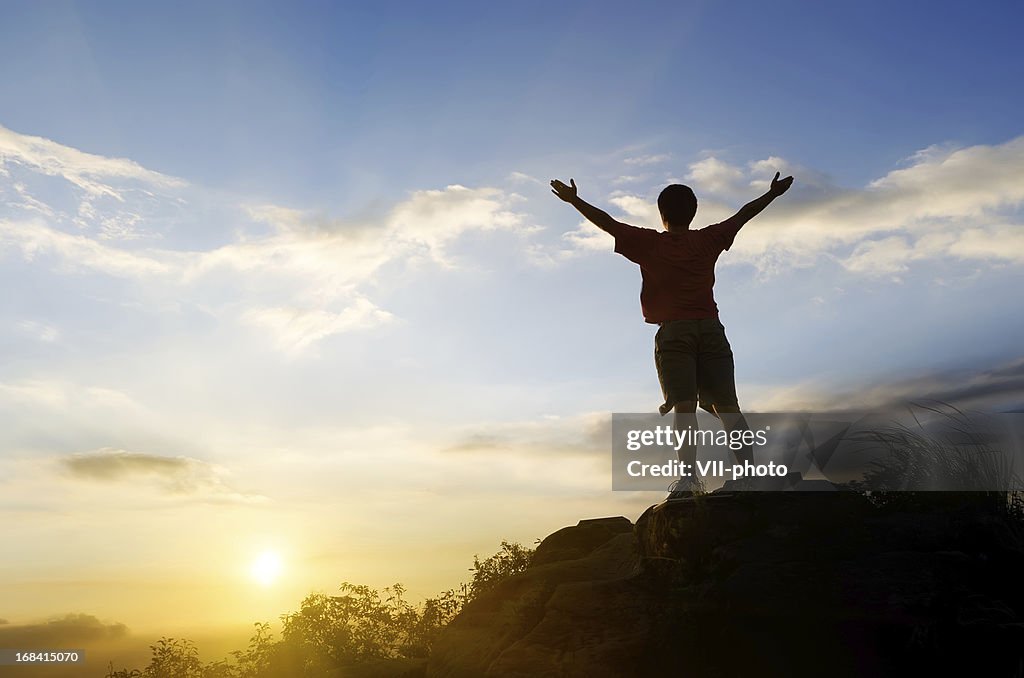 Rear view of a man standing on a rock at sunset feeling free