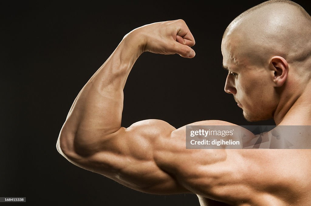 Culturista dobrando biceps em fundo preto
