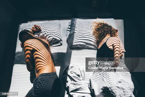 middle-aged couple after a quarrel lies back-to-back on the bed. - separation stock pictures, royalty-free photos & images