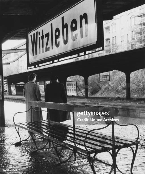 Original-Bildunterschrift: Im strömenden Regen müssen die Fahrgäste stehend auf den Zug warten, denn die Bänke für den ncht überdachten Bahnsteigen...