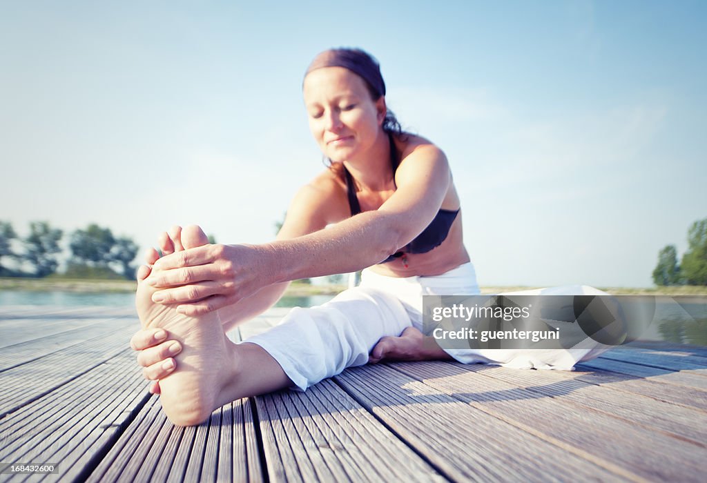 Woman is stretching her legs on a dock