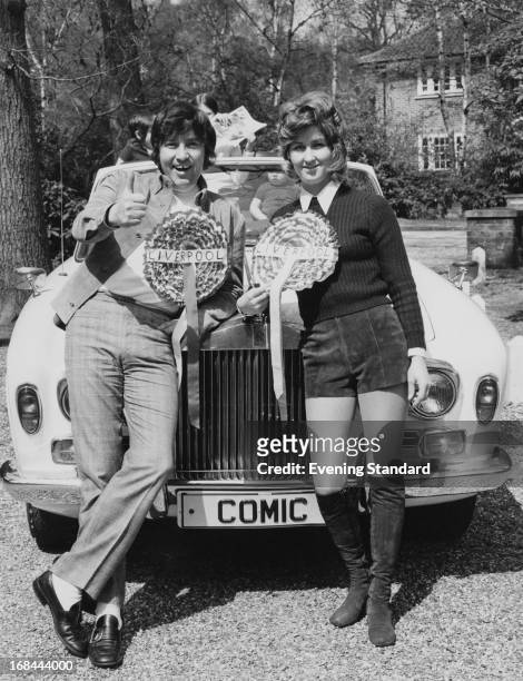 English comedian Jimmy Tarbuck and his wife Pauline leaning on the bonnet of his Rolls Royce , May 1971. Both are wearing outsize Liverpool Football...