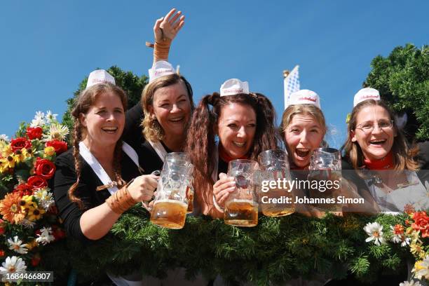 Waitresses wave with beer mugs during the horse coaches parade on the opening day of the 2023 Munich Oktoberfest on September 16, 2023 in Munich,...