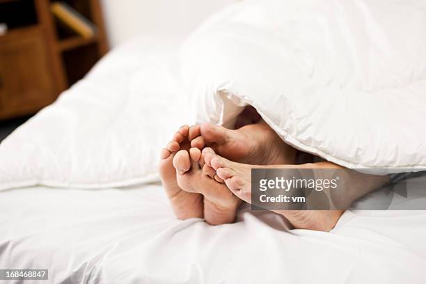 four feet sticking out from underneath blankets - old lady feet stockfoto's en -beelden